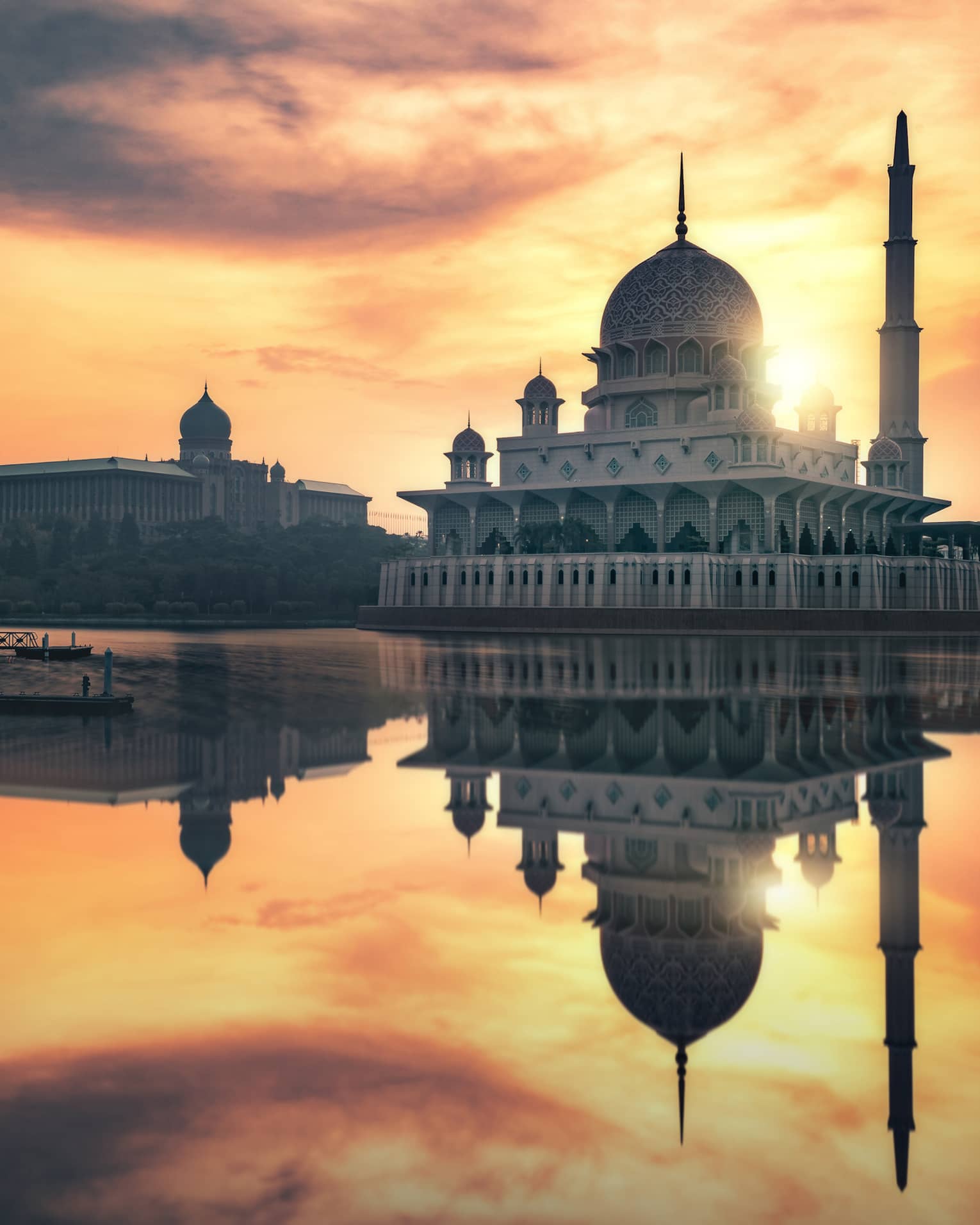 A stunning domed mosque and towering minaret are reflected in the still waters below during a radiant multi-hued sunset.
