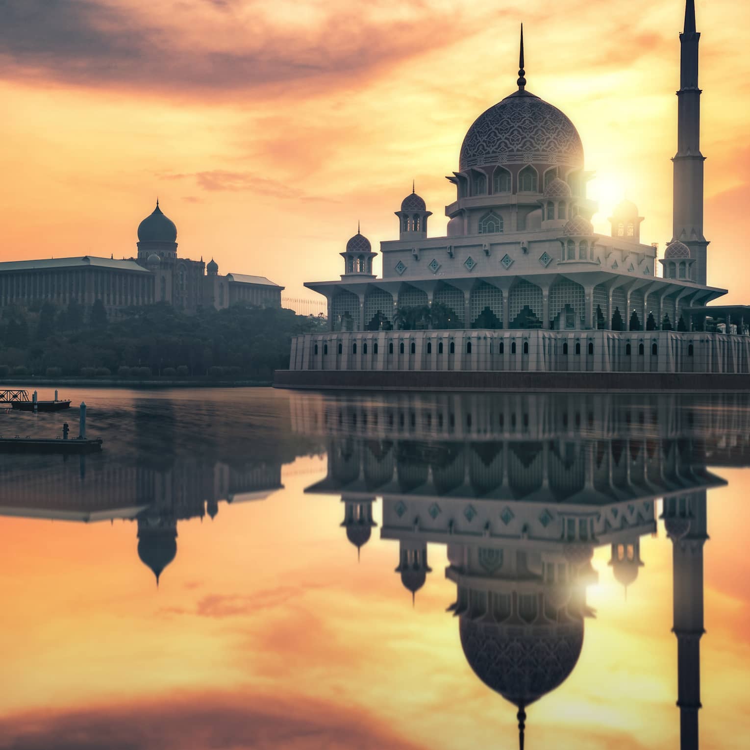 A stunning domed mosque and towering minaret are reflected in the still waters below during a radiant multi-hued sunset.