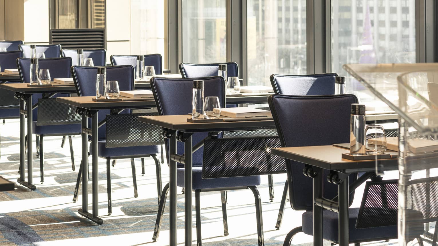Two rows of tables with dark blue chair, glasses and notebook set up for meeting