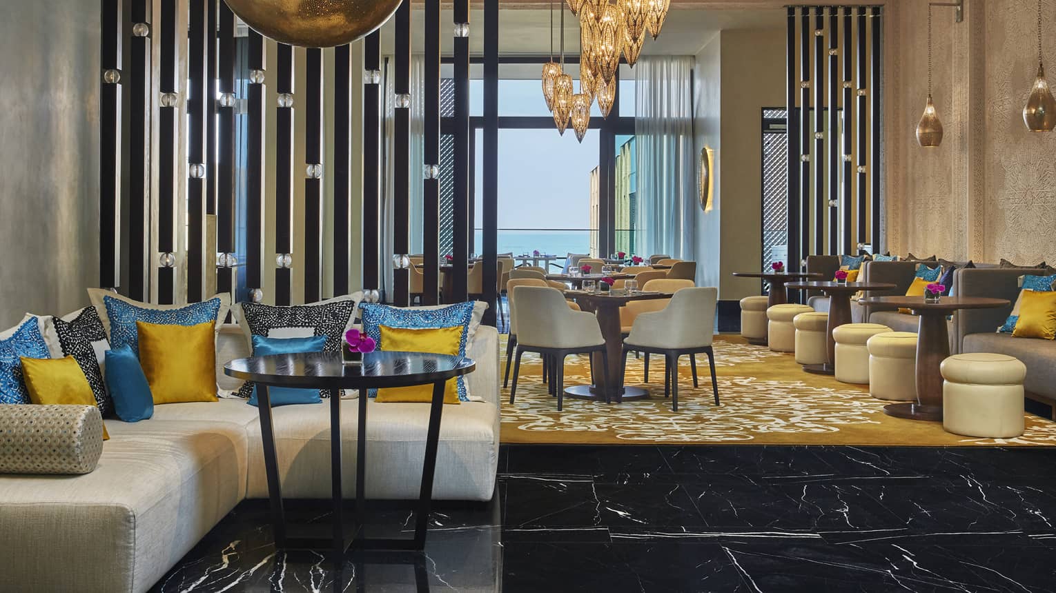 Mint restaurant sofa with bright blue and yellow silk pillows, dining room, large brass lamps and lanterns