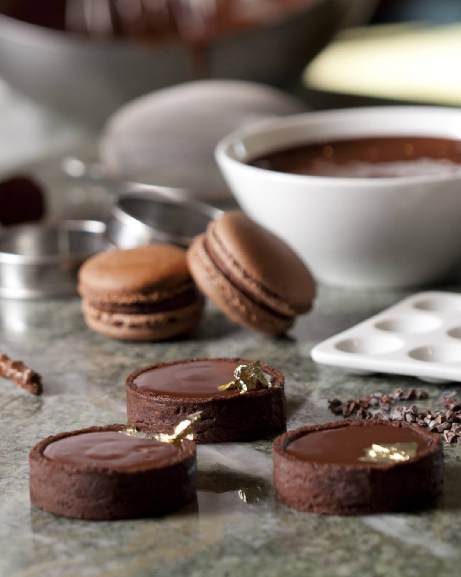 Close-up of fine chocolates, macarons, bowl of melted chocolate on counter