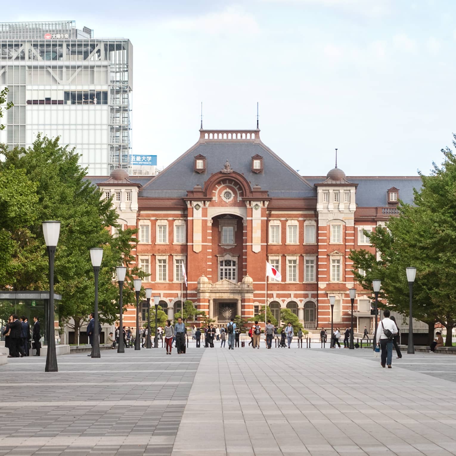 Long view down street-lantern bordered plaza towards Tokyo Station, people strolling in the plaza, tall buildings beyond.