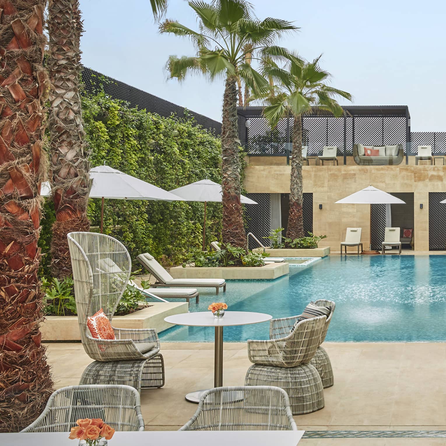 Courtyard pool flanked by tables and chairs with umbrellas, palm trees