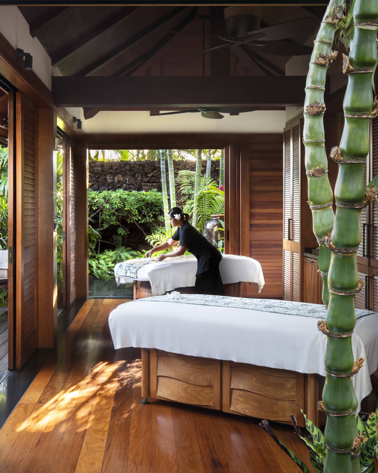 Spa staff spreads sheet on couples massage beds on open-air pavilion