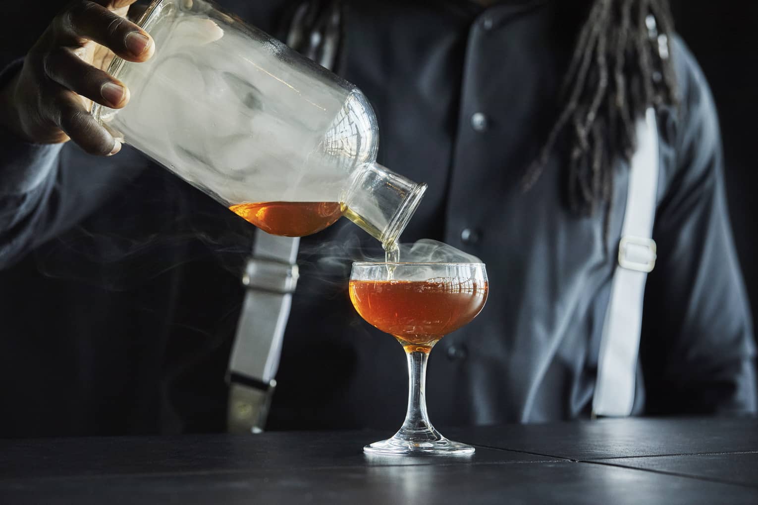 Smoke rolls off the decanter as a Four Seasons staff member pours bourbon into a coupe glass