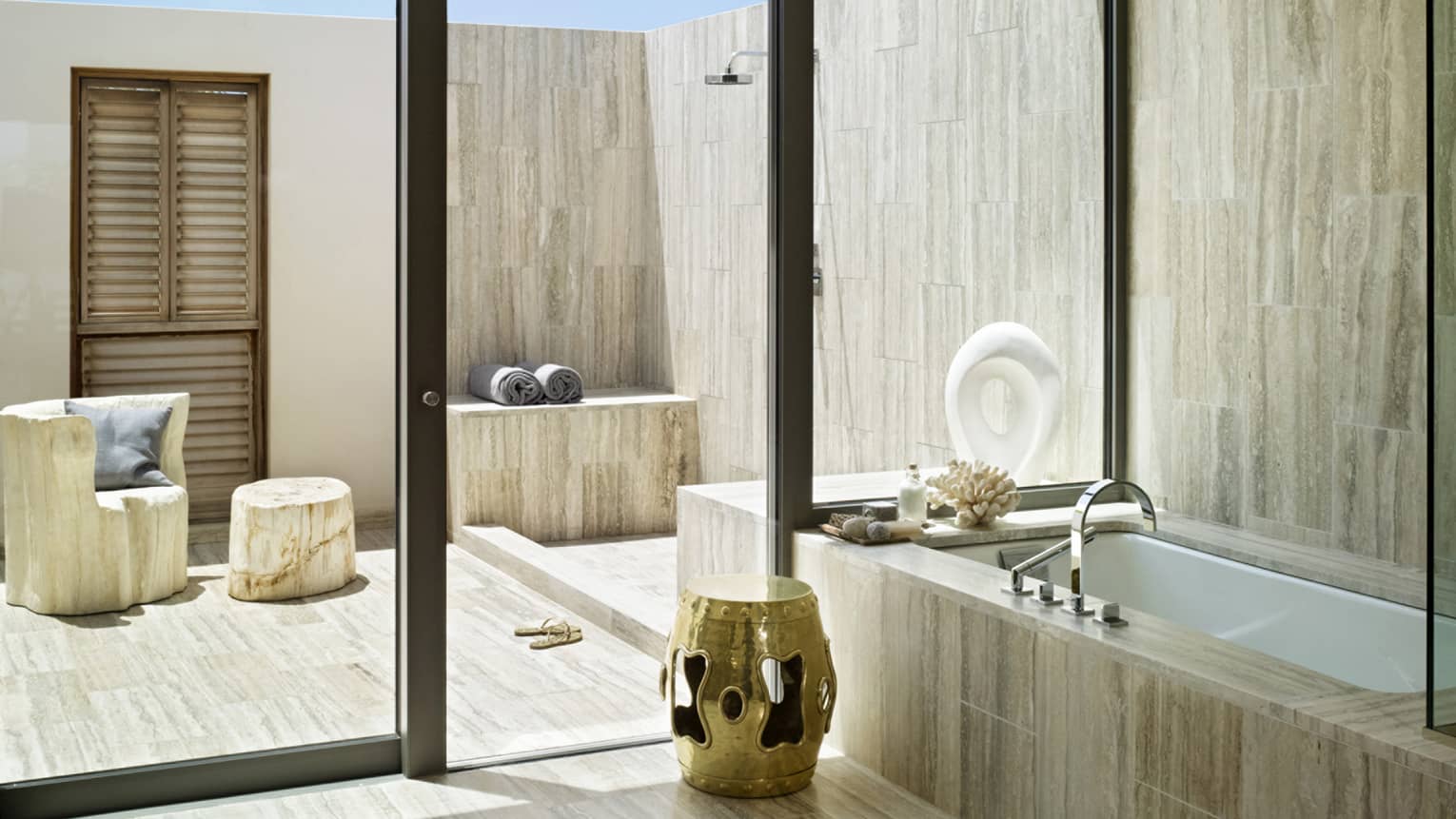 Luxury bathroom with a deep soaking tub and private outdoor shower, featuring natural stone and gold accent decor.