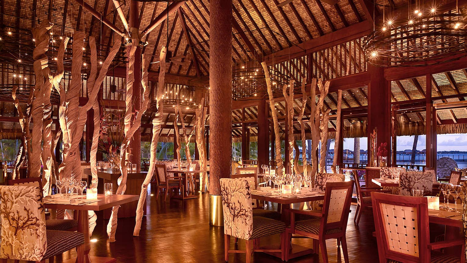Elegant, candle-lit Arii Moana open-air dining room with plush chairs, decorative branches