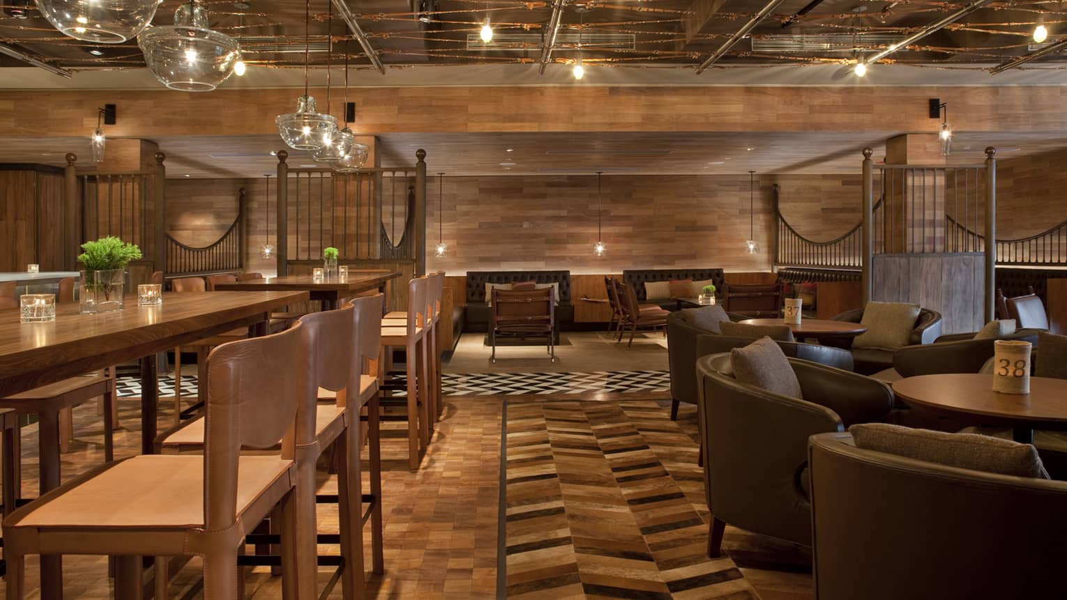 Pony Line lounge with rich brown wood flooring and walls over tables with stools, leather chairs, glass chandeliers