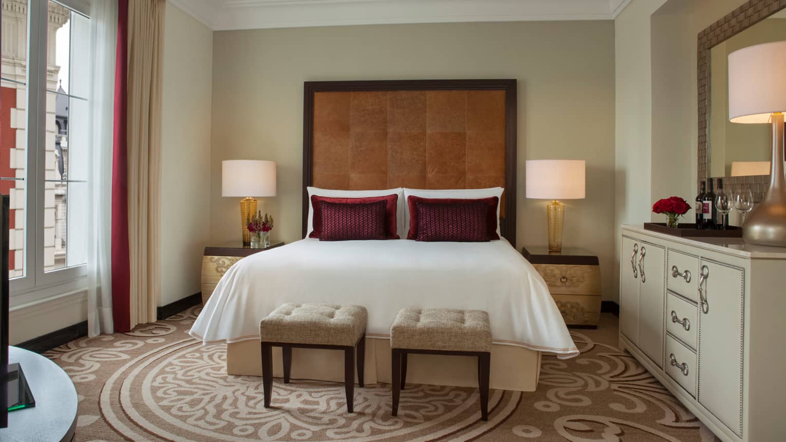 E-Lounge Junior Suite bed with tall brown leather headboard, two small plush beige stools at foot, beige patterned carpet