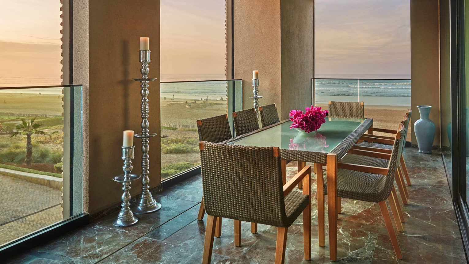 Balcony dining table with wicker chairs, fresh pink flowers, tall silver pillar candles, ocean views
