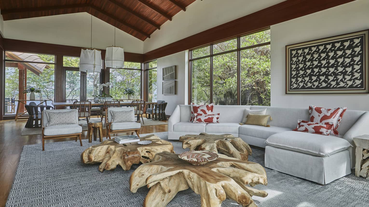 Villa living room with large reclaimed wood coffee tables, curved white sectional sofa, dining room under cathedral wood ceilings