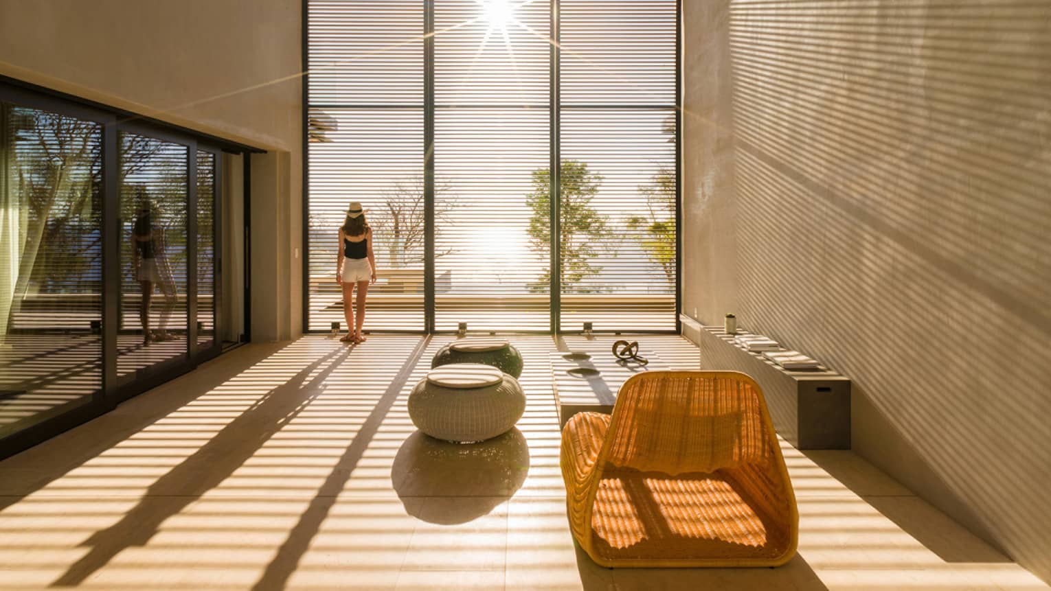 Woman stands by sunny floor to ceiling window in modern room