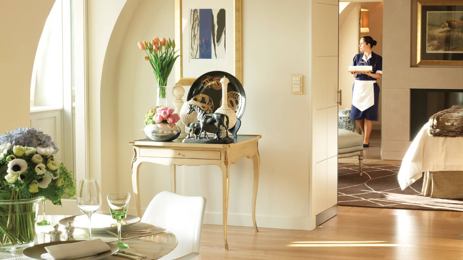 Presidential Suite Loft sunny table with fresh flowers, horse statue, vases, hotel staff walks by bed in background