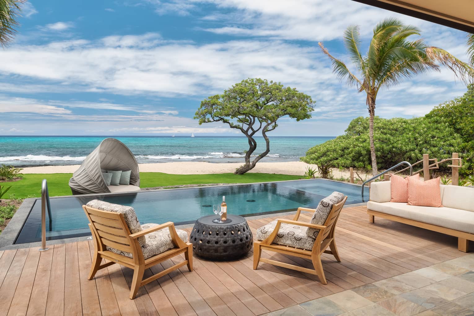 Wooden deck with two chairs and sofa, infinity pool and view of Hawaiian beach