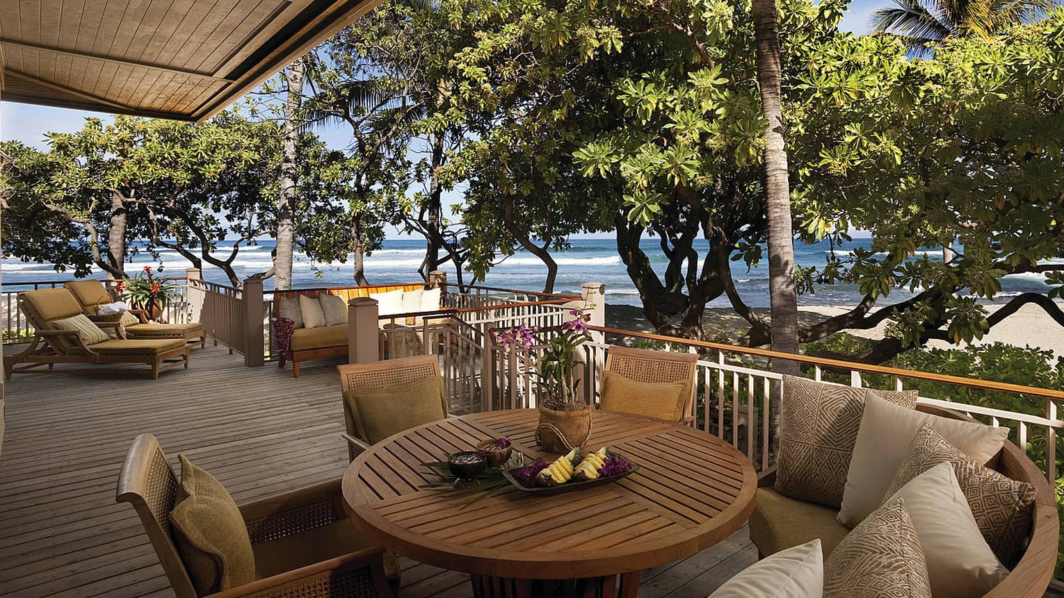 Kailani Suite round wood patio table, cushioned chairs on deck by trees