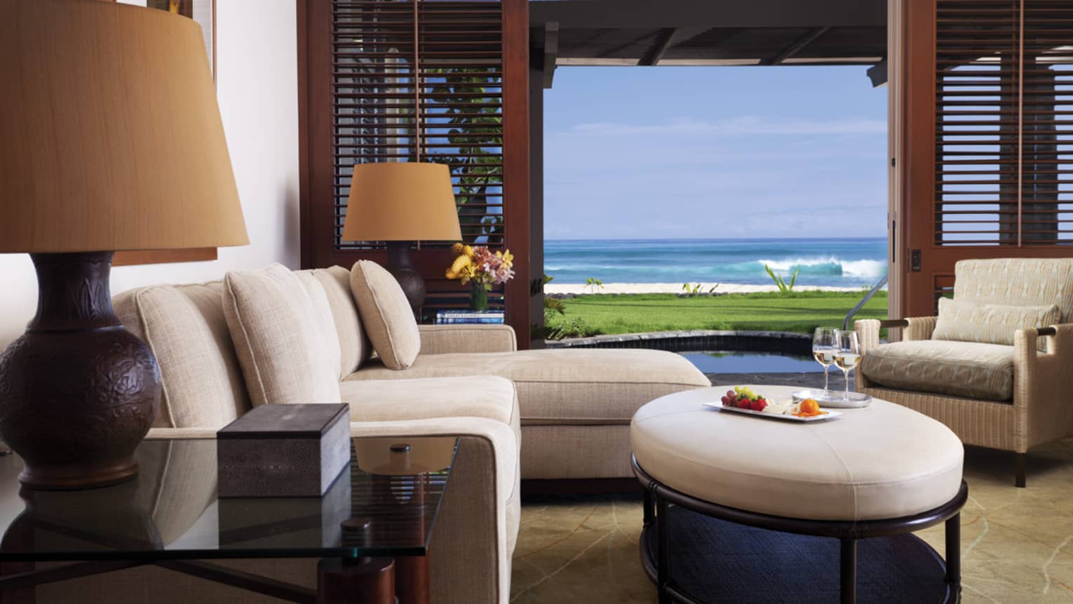 ‘Anelakai Suite plush white chaise, round leather footstool by open wood patio shutters