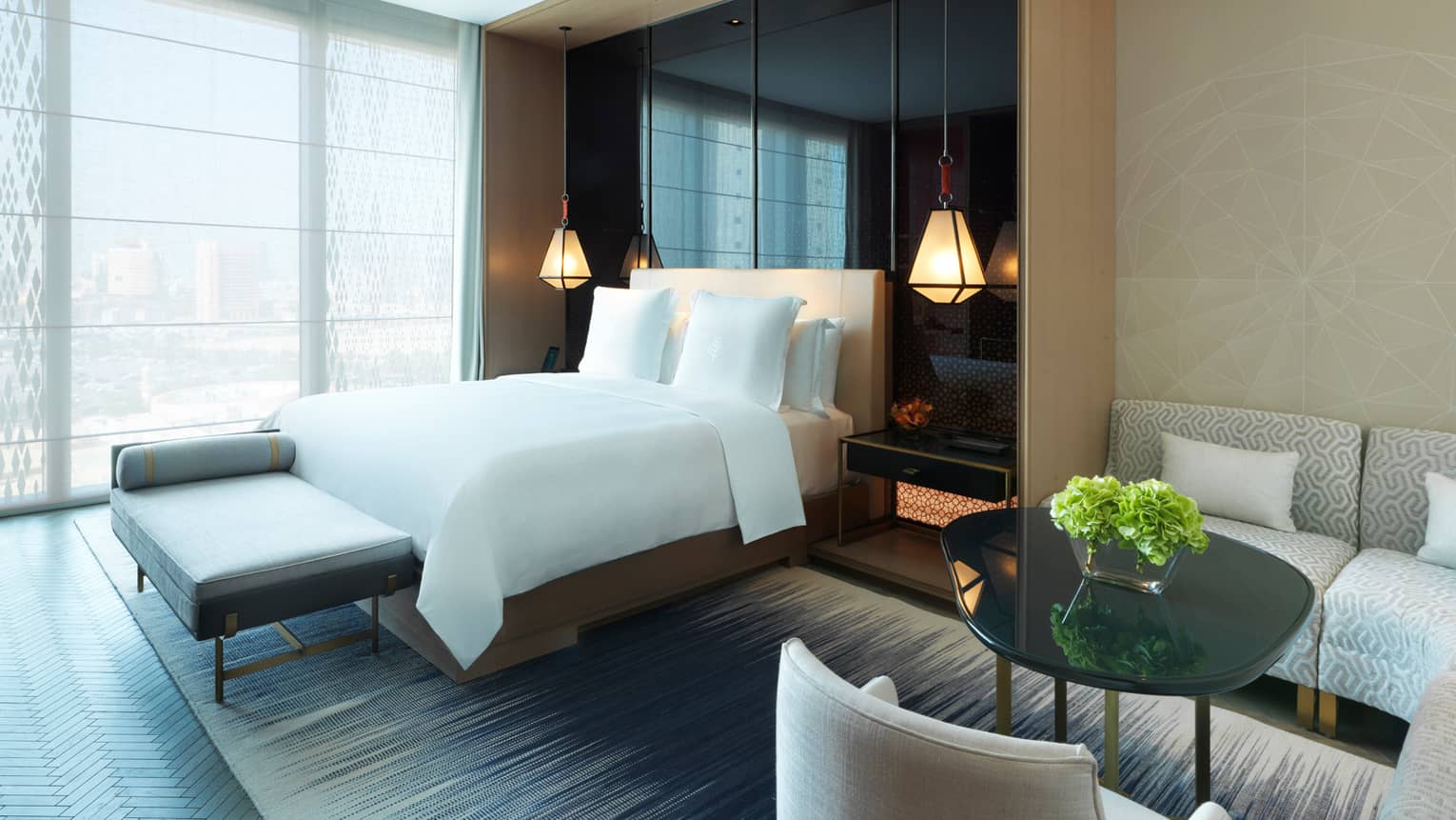 Deluxe Room small dining table, bed, modern chaise at foot in front of sunny floor-to-ceiling window