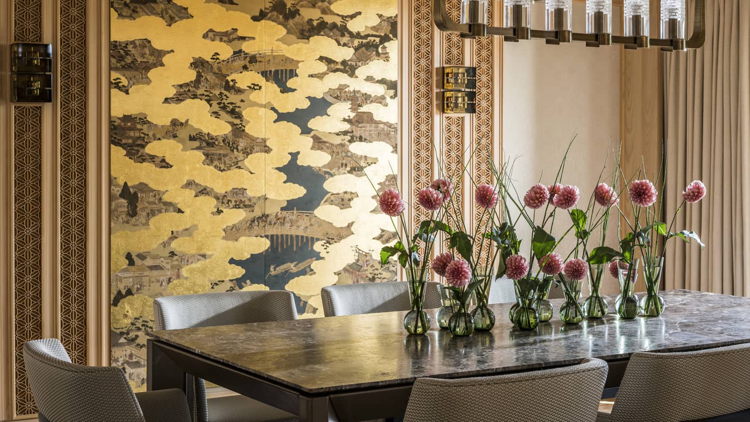 Elegant dining area with a large table decorated with pink flowers in small vases and a gold-accented wall panel