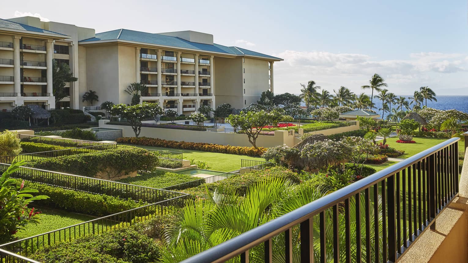 Balcony view of resort buildings with landscaped gardens, palm trees and ocean in the background