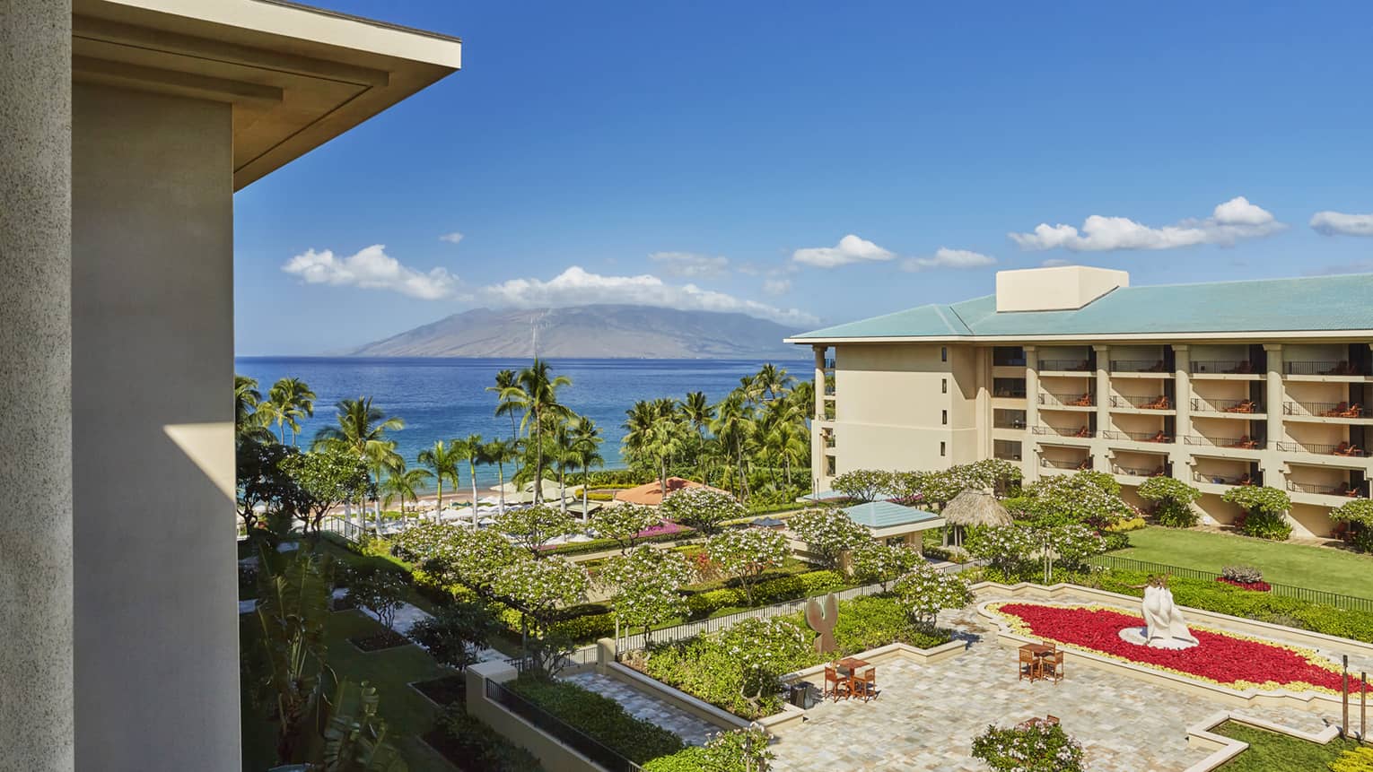 Resort courtyard with gardens and fountain overlooking palm trees beach and ocean with mountain in the distance