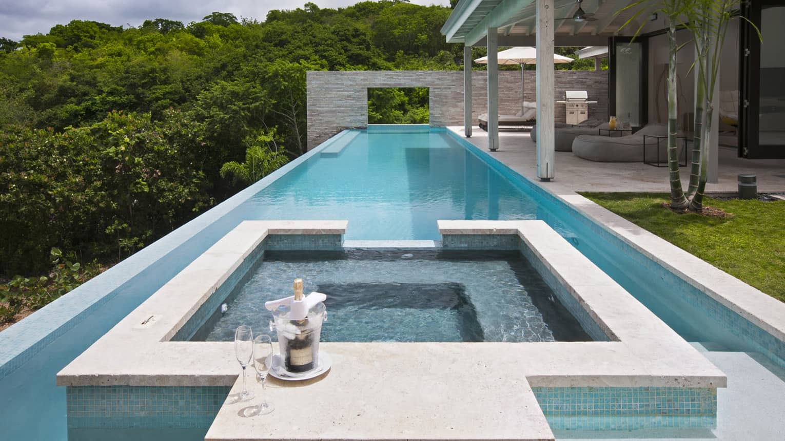 Champagne, two glasses on edge of residence whirlpool, long outdoor swimming pool