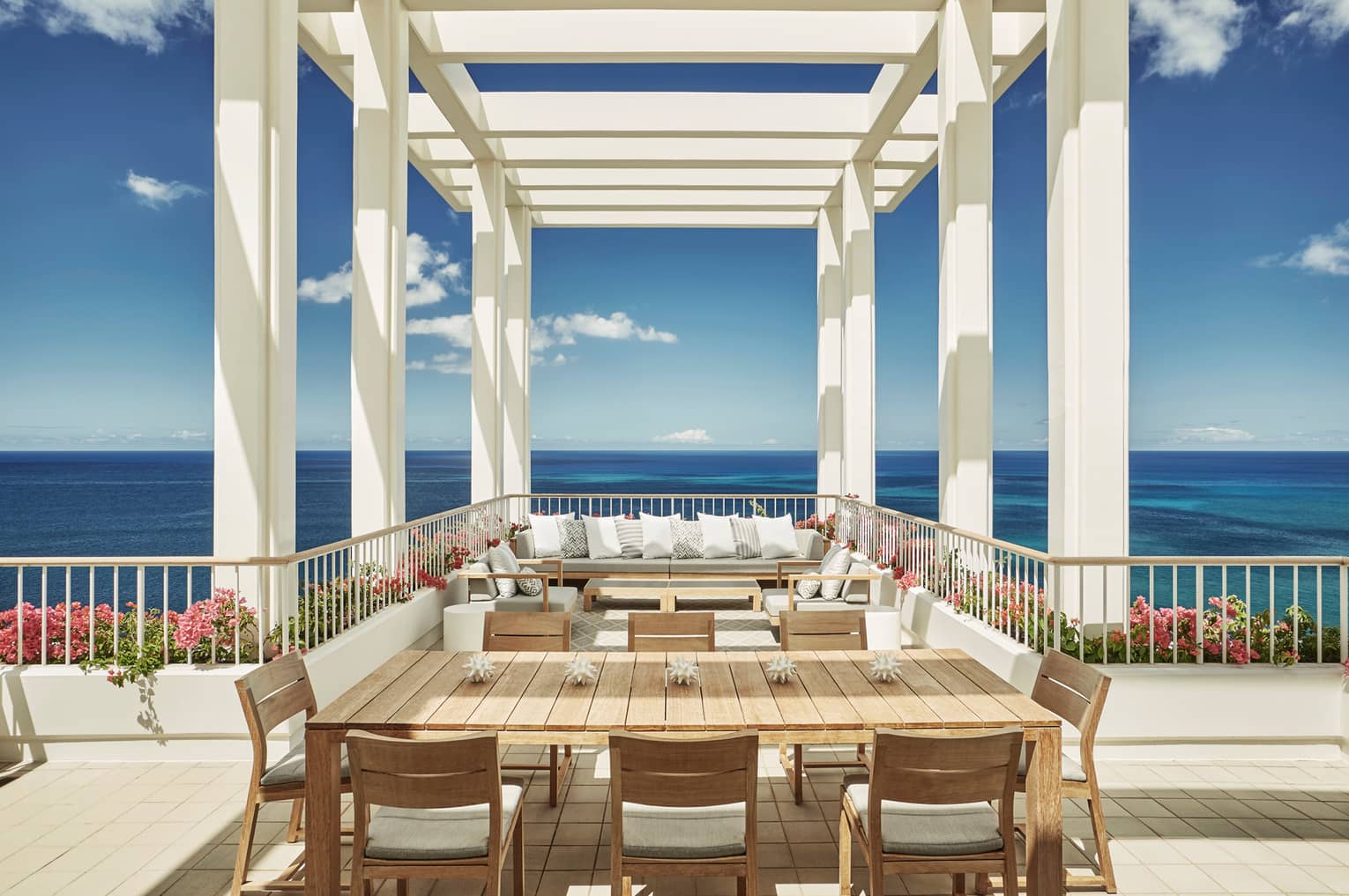 Penthouse Suite large patio dining table, seating area under white pergola, blue sky