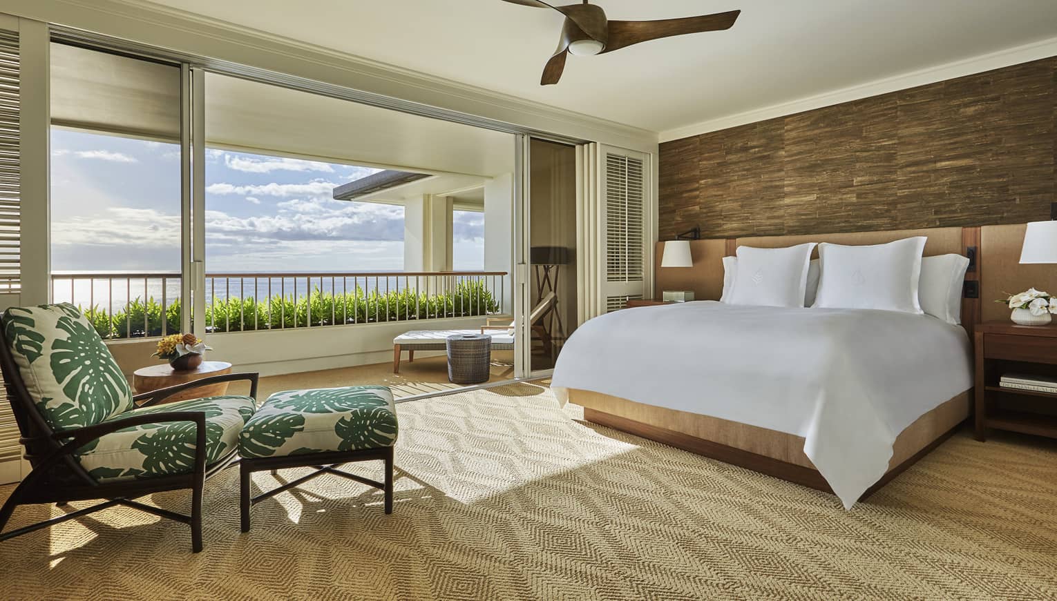 Hotel room bed and tropical print armchair by open air wall to patio, ocean view