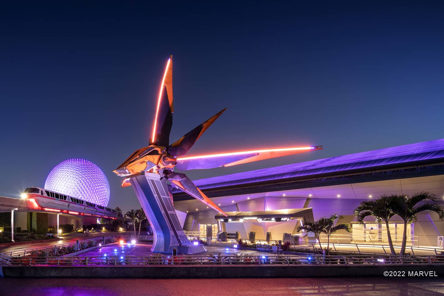 An orange and black sci-fi spaceship resting on a tall pedestal with a tram moving near it.