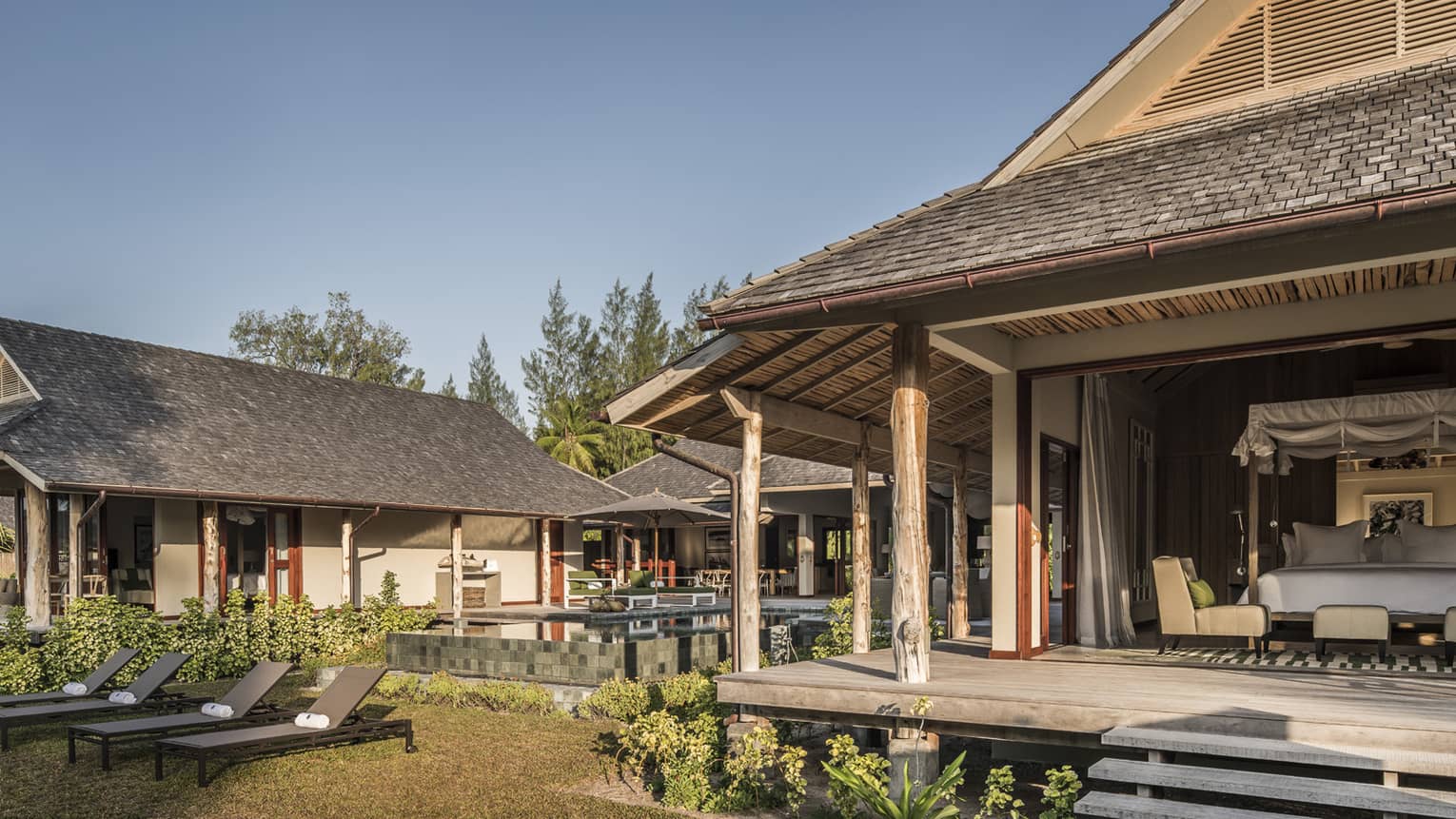 View of bungalow patio, open wall to bedroom from lawn with lounge chairs