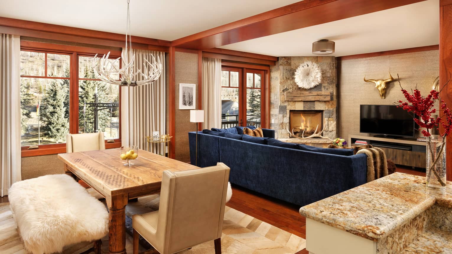 Antler chandelier over dining table with shag bench near blue sofa, fireplace