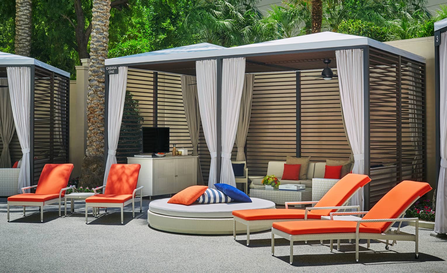 Orange deck chairs, large plush ottoman by poolside cabana with sofas, TV