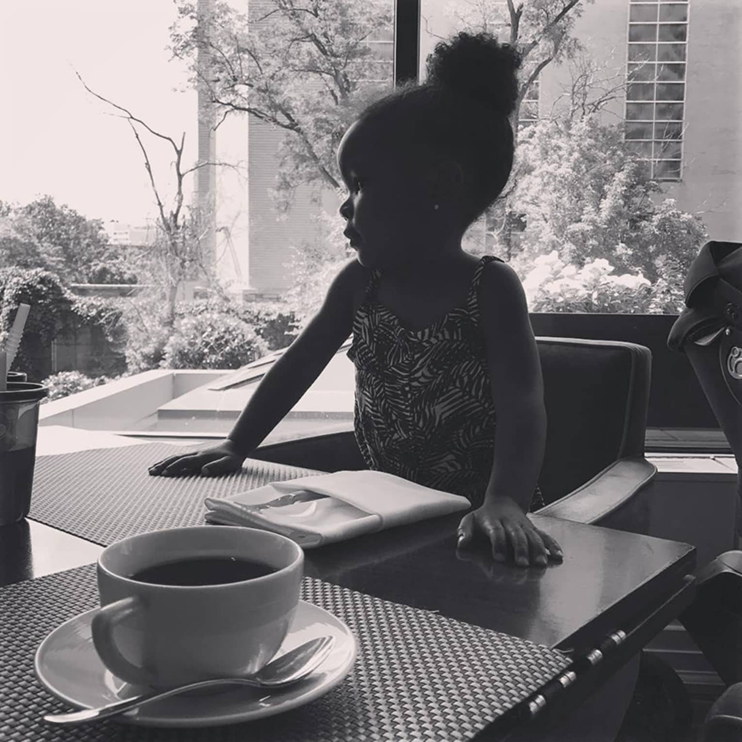 Coffee cup on dining table across from little girl in chair, window