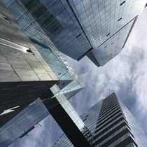 Upward view of modern glass skyscrapers connected by a glass bridge, set against a cloudy sky
