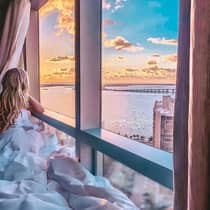 Young girl looks through large window over water, sunrise