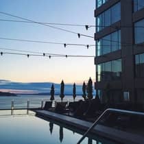 Silhouettes of patio chairs, closed umbrellas around outdoor swimming pool at sunrise