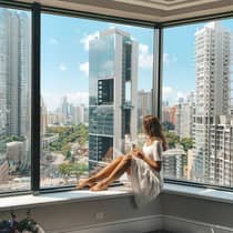 Woman lounges in hotel room corner window overlooking city