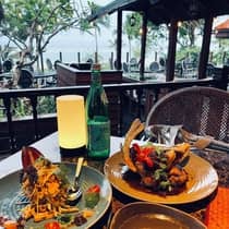 Colorful plates of food are served on a restaurant patio with an ocean view