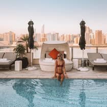 Woman wearing bathing suit sits on edge of outdoor swimming pool, lounge chair