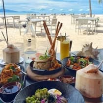 A table on the beach filled with various colourful culinary dishes, coconuts and juice