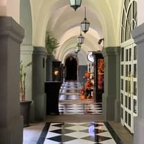 An arched hallway with black and white checker tiles and steel lanterns hanging from the ceiling.