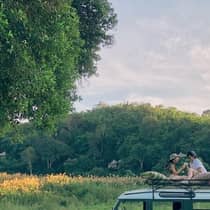 Two guests sit on top of a safari vehicle in a field
