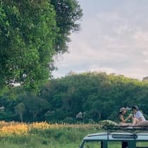 Two guests sit on top of a safari vehicle in a field