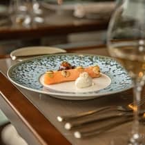 A delicate salmon fillet garnished with dollops of cream, microgreens and thinly sliced vegetables, presented on a speckled blue and white plate