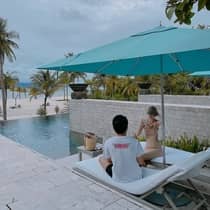 A couple sitting on lounge chairs enjoys refreshments by the pool under a blue umbrella