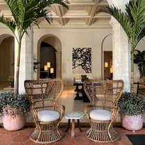 Elegant seating area featuring two wicker chairs with cushions and a small table between them, framed by stone arches and tall potted plants in a luxurious setting.