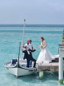 Groom helps bride into canoe at dock of overwater wedding ceremony on lagoon