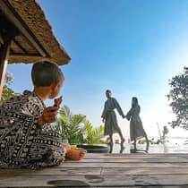 Family wearing robes, young child sits cross legged on patio as parents hold hands in background