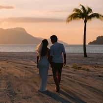 A newlywed couple walks on the beach at sunset