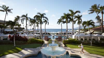 Historic 1990s photo of staff carrying towels past large fountain to outdoor pool, deck at resort