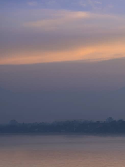 The sun rises as a single boat floats by in front of the mountains